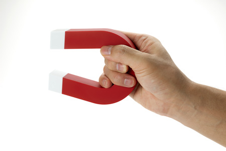 A hand holding a magnet isolated on white to pick up an objectの写真素材