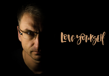 Love yourself. Inspirational quote. Handwritten text, modern calligraphy. Close-up portrait of man in glasses. Black backgroundの写真素材