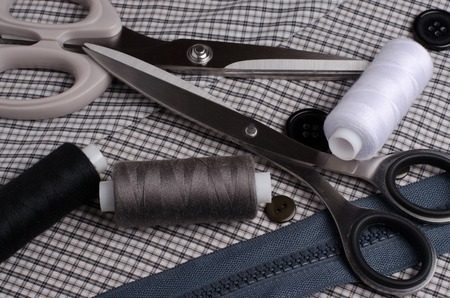 Tools and accessories for sewing. Sewing thread, scissors, buttons, zipper on gray textile background. Close upの写真素材