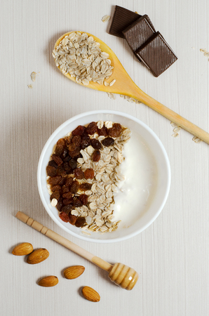 Oatmeal with raisins and yogurt. Oatmeal in the wooden spoon. Almond, chocolate. Flat top view. On a white tableの写真素材