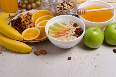 Healthy food. Fruit, homemade granola, nuts, oatmeal, honey, orange juice on a white table. Side viewの写真素材