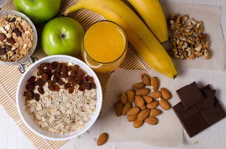 Healthy food. Fruit, homemade granola, nuts, chocolate, oatmeal, orange juice on a white table. Flat top viewの写真素材