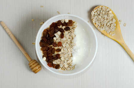 Oatmeal with raisins and yogurt. Oatmeal in the wooden spoon. Flat top view. On a white tableの写真素材