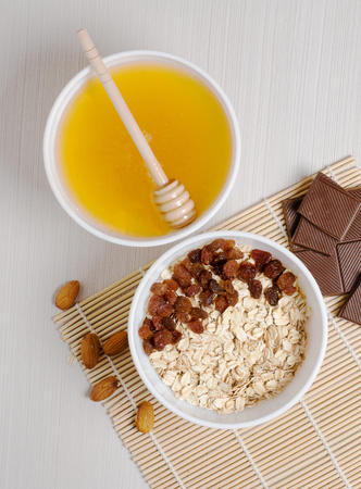 Oatmeal with raisins on the tablecloth from bamboo. Honey, chocolate, almonds. Flat top viewの写真素材