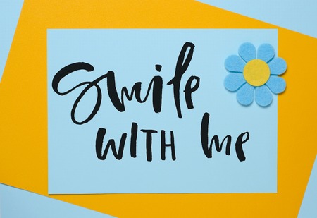 Smile with me. Handwritten text. Inspirational quote.  Blue flower made of felt on a blue and orange backgroundの写真素材