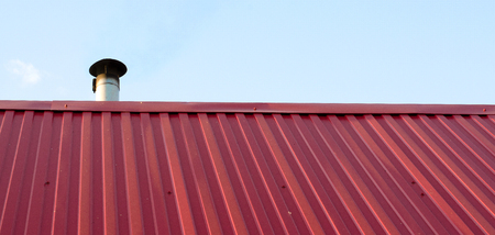 Tiled roof top with chimney with blue cloudy sky in background. Smoke raising from a chimney. Horizontal photoの写真素材