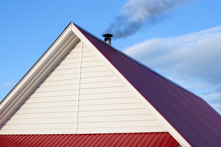Tiled roof top with chimney with blue cloudy sky in background. Smoke raising from a chimney. Summer, noon.の写真素材