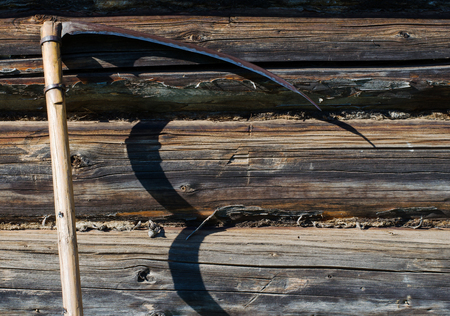 Garden tool - scythe. Wall of the rural house made from wooden logsの写真素材