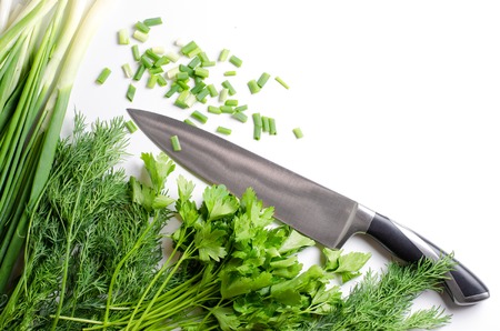 Green onions, dill, parsley, kitchen knife on white background. Flat top view
