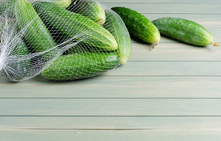 A lot of green cucumbers in net bag. Light wooden background. Space for textの写真素材