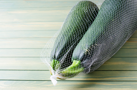 Two large green zucchini in a mesh bag. Wooden background. Copy space.の写真素材
