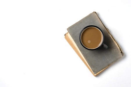 An old book with a torn cover. Coffee with milk. White background. Flat top view. Space for text