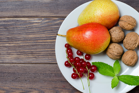 Vegetarian food. Ripe pears, walnuts, red currant, mint leaves on a white round plate. Flat top viewの写真素材