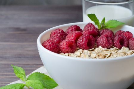 Healthy vegetarian food. Oatmeal with raspberryand mint leaves. Brown wooden background.の写真素材