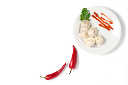 Traditional Russian dumplings, ravioli, dumplings on a white plate with red sauce and parsley. White background. Red chilli pepperの写真素材