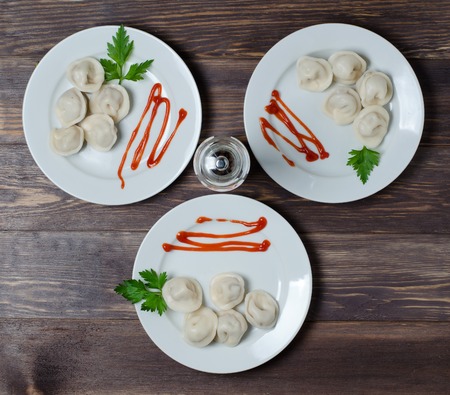 Traditional Russian dumplings, ravioli, dumplings on a white plate with red sauce and parsley. Dark wooden background.の写真素材