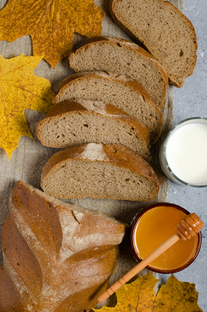 Rye bread is cut into pieces. Honey, milk in a glass Cup, yellow maple leaves. Traditional rural food. Vertical photoの写真素材