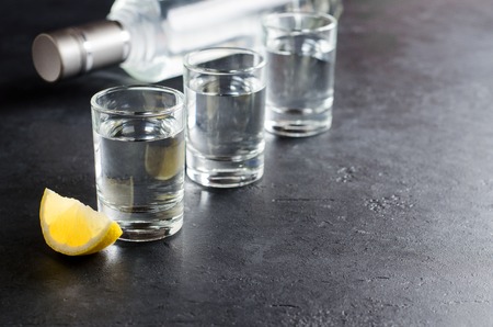 Three glasses, a bottle of vodka, a piece of lemon on a dark background. Copy spaceの写真素材