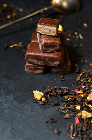 Chocolates and black tea with herbs. Metal tea strainer. Dark background. Copy space. Vertical photoの写真素材