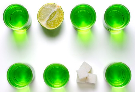 Absinthe green liquor in glasses. Alcoholic hallucinogenic beverage. White background. Pieces of...