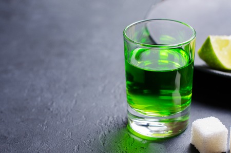 Absinthe green liquor in glasses. Alcoholic hallucinogenic beverage. Dark background. Pieces of lime and white sugar. Copy spaceの写真素材