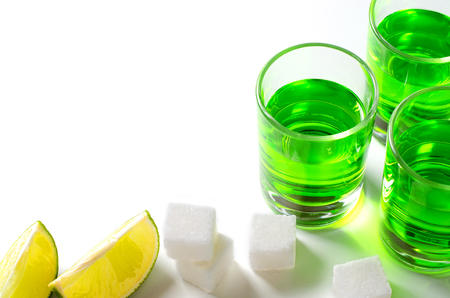 Absinthe green liquor in glasses. Alcoholic hallucinogenic beverage. White background. Pieces of lime and white sugar. Copy spaceの写真素材