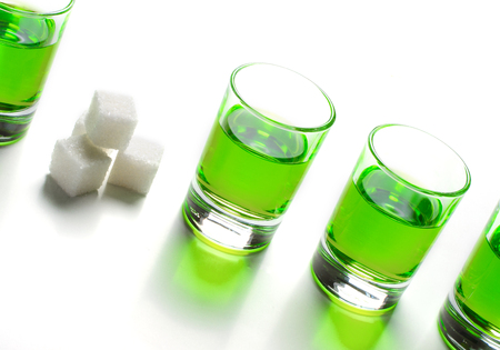 Absinthe green liquor in glasses. Alcoholic hallucinogenic beverage. White background. Pieces of white sugar. Copy spaceの写真素材