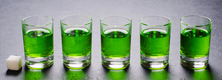 Absinthe green liquor in glasses. Alcoholic hallucinogenic beverage. Dark background. Pieces of white sugarの写真素材