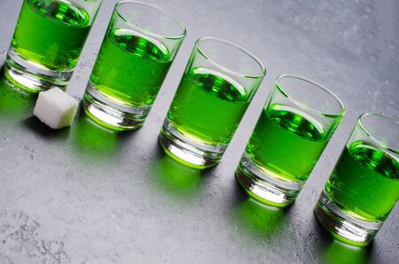 Absinthe green liquor in glasses. Alcoholic hallucinogenic beverage. Dark background. Pieces of white sugarの写真素材