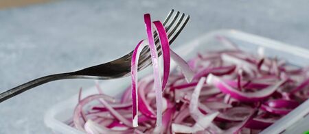 Pickled chopped red onion in vinegar in a plastic container. A delicious side dish for meat and fish dishes. Light grey background.の写真素材