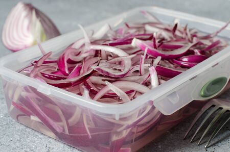 Pickled chopped red onion in vinegar in a plastic container. A delicious side dish for meat and fish dishes. Light grey background.の写真素材