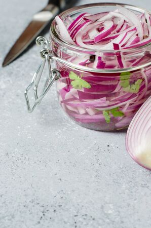 Pickled chopped red onion in vinegar in a glass jar. A delicious side dish for meat and fish dishes. Light grey background.の写真素材