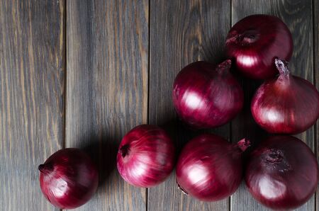 Lots of red onions on a brown wooden background. Red onions on old crumpled burlap. Copy space. Flat top viewの写真素材