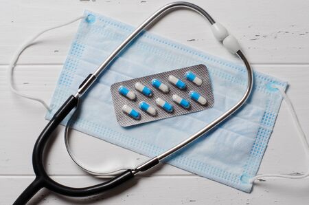 Medical disposable mask, tablets, stethoscope on a white background. The concept of protection during an epidemic of the disease. Copy space. Flat top view.の写真素材
