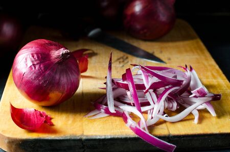 Red onion and sliced onion on a wooden chopping Board. Side view.