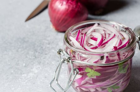 Pickled chopped red onion in vinegar in a glass jar. A delicious side dish for meat and fish dishes. Light grey background.の写真素材