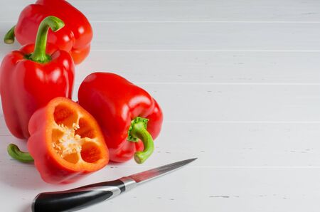 Red ripe bell peppers and a kitchen knife. White wooden background. Copy spaceの写真素材