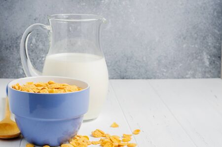 Corn flakes and milk in a glass jug. White wooden table. Copy space.の写真素材