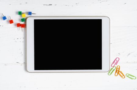 A tablet with an empty screen and office supplies on a white wooden background. Concept app for...