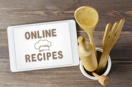 Online recipes. Cookbook in a tablet computer. Kitchen utensils. Brown wooden background.の写真素材
