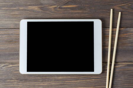 A tablet computer and chopsticks on a brown wooden background. Copy space. Concept of cooking recipesの写真素材