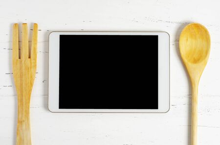 A tablet computer and cooking battery on a white wooden background. Copy space. Concept of cooking recipesの写真素材