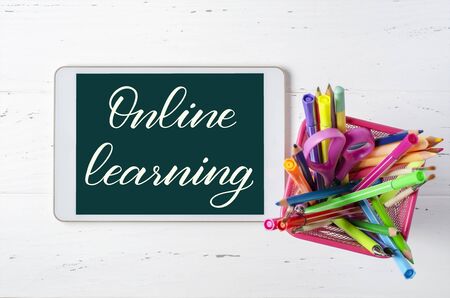 Online learning - handwritten inscription on a tablet. The concept of distance training for children. Tablet and office supplies on a white wooden backgroundの写真素材