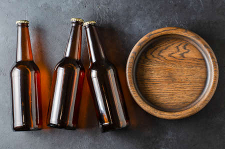 Beer in glass bottles and a wooden plate for snacks. Grey concrete background. Copy space.の写真素材
