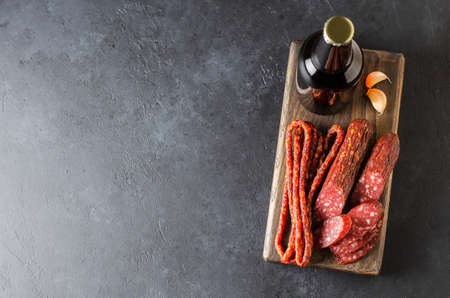 Beer in glass bottles and sausage. Dark concrete background. Copy space