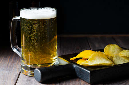 Lager beer in a glass mug. Salted potato chips. Wooden background. Copy space.