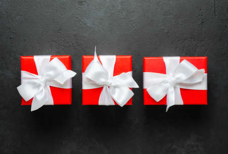 Red gift boxes with white ribbons. Black concrete background. Copy spaceの写真素材