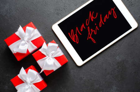 Black Friday - red handwriting on the tablet screen. Gift boxes with ribbons. The concept of holiday salesの写真素材