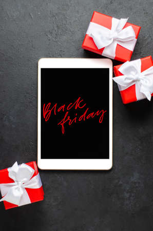 Black Friday - red handwriting on the tablet screen. Gift boxes with ribbons. The concept of holiday salesの写真素材