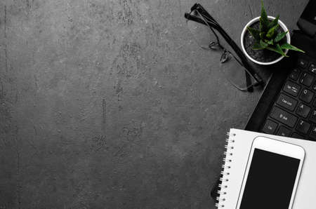 Electronic gadgets, succulent flower and stationery accessories on a black concrete background. Copy...